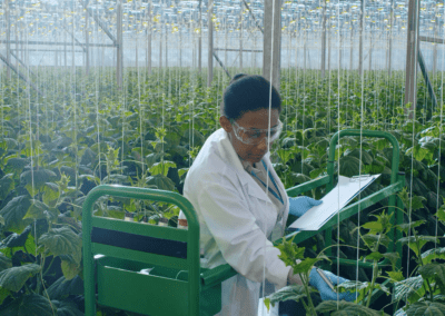 a woman wearing a white lab coat, standing in a greenhouse filled with plants